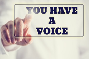 IMAGE: A hand touching a button that has text on it that says 'YOU HAVE A VOICE'.